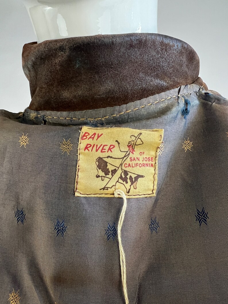 May include: Brown suede jacket with a Bay River label. The label features a cowboy riding a bull and the text "Bay River, of San Jose, California".