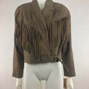 May include: A brown suede jacket with fringe detailing and a belt. The jacket has a  collared neckline and long sleeves.