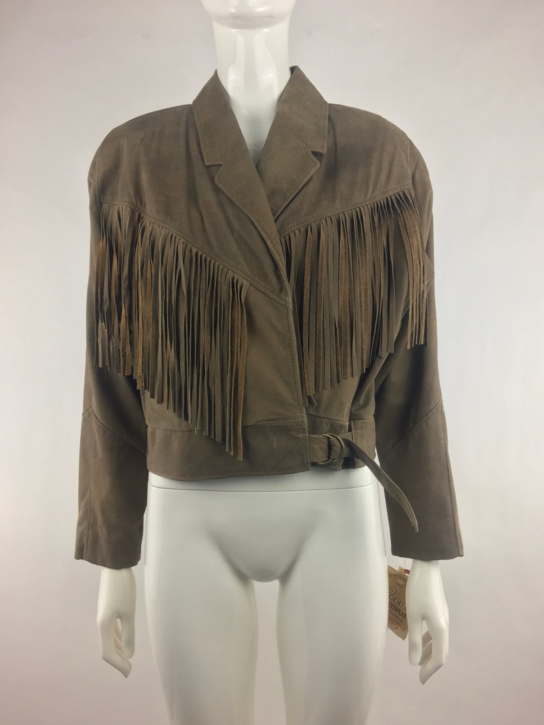 May include: A brown suede jacket with fringe detailing and a belt. The jacket has a  collared neckline and long sleeves.