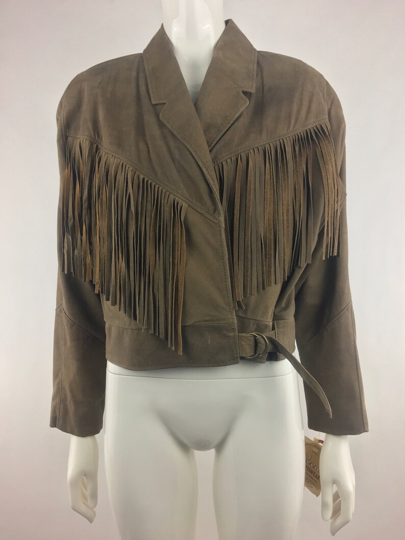 May include: A brown suede jacket with fringe detailing around the collar and hem. The jacket has a belt with a silver buckle.