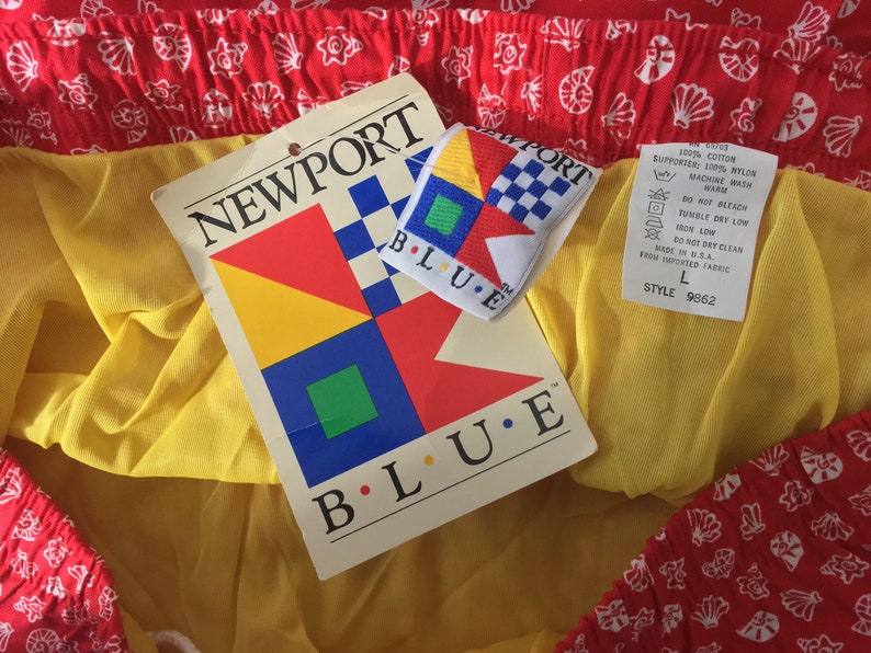 May include: A red and yellow fabric with a white pattern of seashells. The fabric has a tag attached that says "NEWPORT BLUE" and features a colorful geometric design. The tag also includes care instructions and a size label that says "L" and "STYLE 9862".