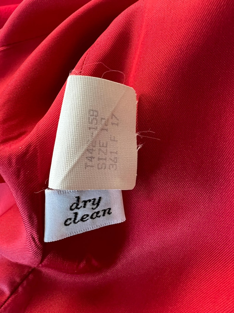 May include: Close-up of a vibrant red fabric with a white tag. The tag reads "dry clean" in cursive and includes size information. The fabric appears to be part of a garment.