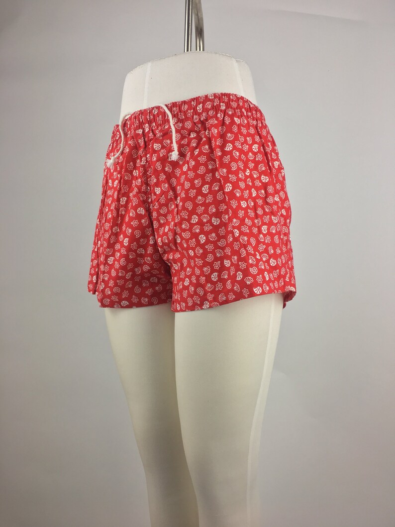 May include: Red shorts with a white floral print. The shorts have a drawstring waist.