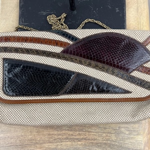 May include: A rectangular clutch bag featuring a beige textured fabric base with geometric panels of dark brown and black snakeskin-embossed leather. The bag includes a thin gold-tone metal chain strap and is finished with brown leather piping.