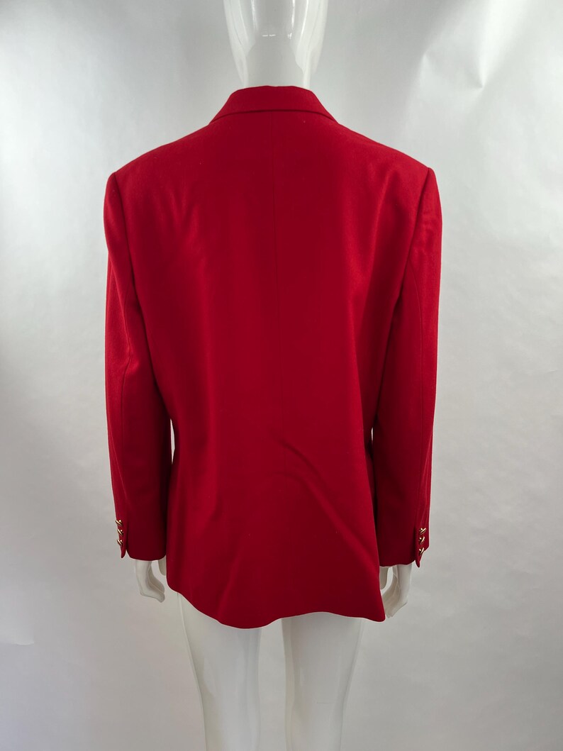May include: A vibrant red blazer with gold-colored buttons on the sleeves. The back view of the blazer shows a classic tailored design. The blazer is displayed on a mannequin.