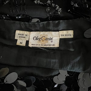 Op de afbeelding: Zwart top met pailletten met een label met de tekst "Oleg Cassini" en "Made in China" in maat "M" en RN 62313.