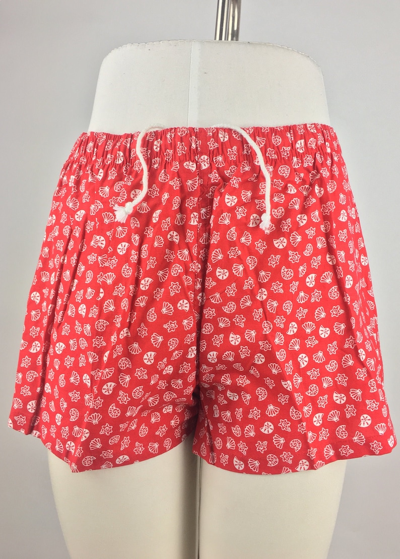 May include: Red shorts with a white seashell pattern. The shorts have a drawstring waist.