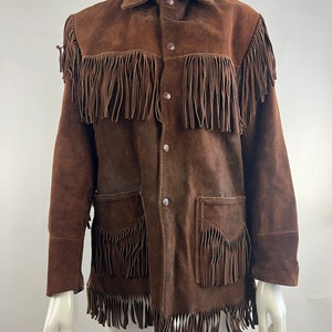 May include: A brown suede jacket with fringe detailing on the front, collar and sleeves. The jacket has a button-up closure and two flap pockets.