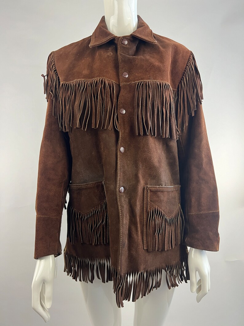 May include: A brown suede jacket with fringe detailing on the front, collar and sleeves. The jacket has a button-up closure and two flap pockets.