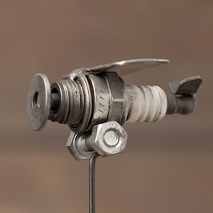 May include: A small metal airplane sculpture made from recycled materials, including a spark plug, nuts, and bolts. The airplane is mounted on a metal stand.