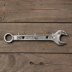 May include: A silver wrench with the text "Mercedes-Benz" on it, mounted on a wooden surface and used as a coat rack.