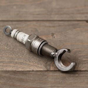 May include: A silver spark plug with a wrench attached to the end. The spark plug is labeled "BOSCH".