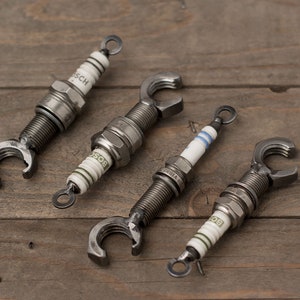 May include: Four spark plugs with metal bottle openers attached to the end. The spark plugs are silver and have the word "BOSCH" printed on them.