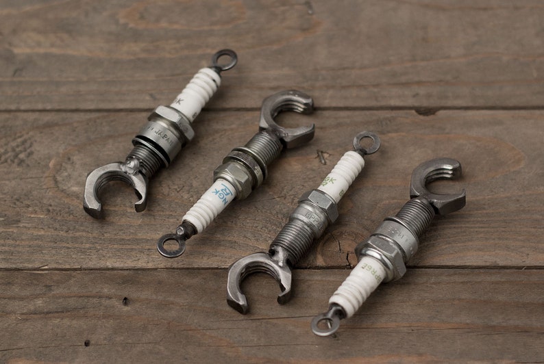 May include: Four silver spark plug bottle openers with a metal loop at the top. The spark plugs are labeled with the text "NGK" and "BP7ES".