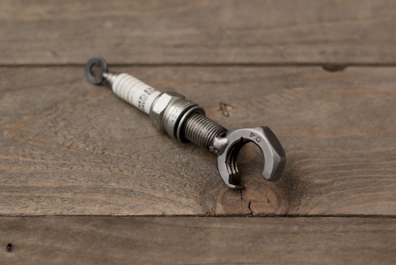 May include: A silver bottle opener made from a repurposed spark plug. The opener has a nut-shaped handle with the number "04" stamped on it.