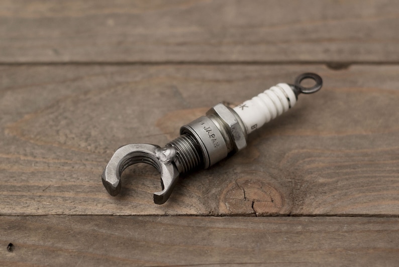 May include: A silver spark plug with a metal wrench attached to the end. The spark plug is labeled "JAPAN".
