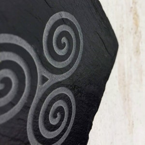 May include: A black slate coaster with a triple spiral design etched into the surface.