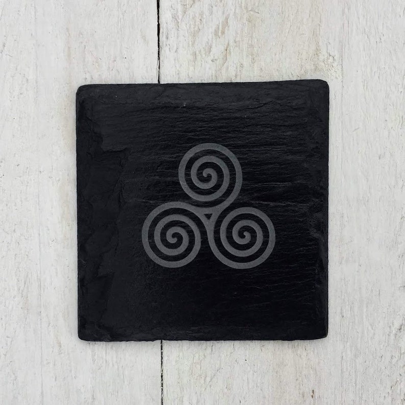 May include: A black slate coaster with a white Celtic knot design. The coaster is square and has a smooth surface.
