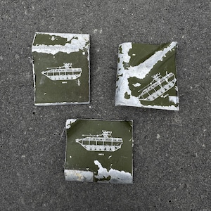 May include: Three weathered, rectangular metal pieces with a green background and a white tank diagram. The metal has peeling paint and a distressed appearance. The tank diagram includes the text "BMP-2".