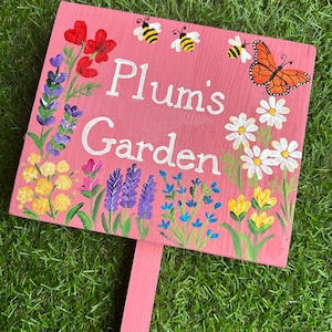 May include: A pink wooden garden sign with the text "Plum's Garden" painted in white. The sign is decorated with painted flowers and bees.