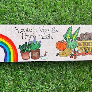 May include: A hand-painted garden sign with a rainbow, two potted plants, a pumpkin, a squash, carrots, and a basket of tomatoes. The sign reads "Rosie's Veg & Herb Patch."