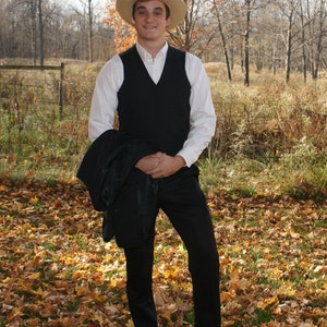 Puede incluir: Un hombre con una camisa blanca, un chaleco negro y pantalones negros est&aacute; de pie en un campo de hojas ca&iacute;das. Lleva un sombrero de paja y tiene una expresi&oacute;n seria en su rostro.