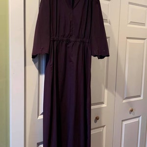 Puede incluir: Un vestido largo de color morado oscuro con cintura fruncida y mangas acampanadas. El vestido tiene un dise&ntilde;o simple y elegante.