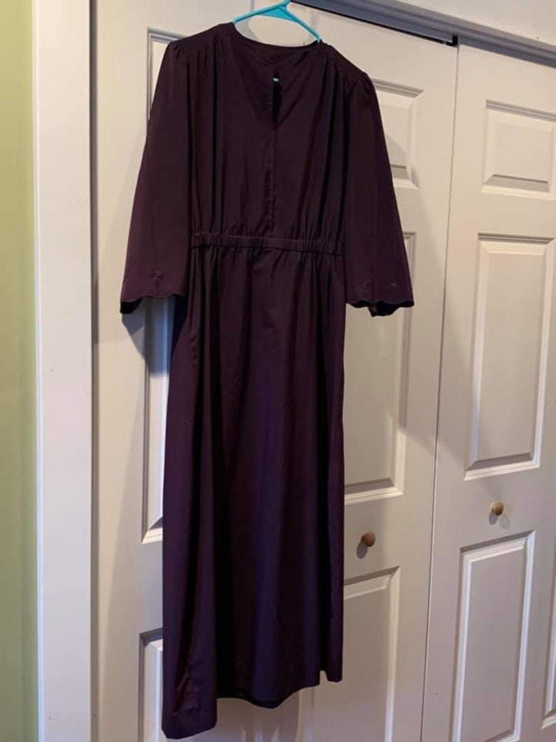 Puede incluir: Un vestido largo de color morado oscuro con cintura fruncida y mangas acampanadas. El vestido tiene un dise&ntilde;o simple y elegante.