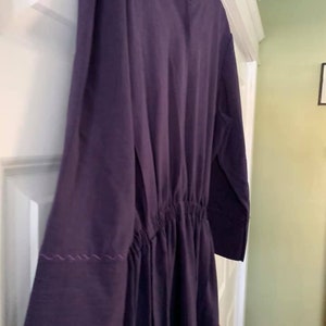 Puede incluir: Un vestido largo de manga larga, de color morado oscuro, con cintura fruncida y un peque&ntilde;o detalle cosido en los pu&ntilde;os.