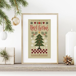 Pode incluir: Um padrão de ponto cruz emoldurado sobre fundo bege com o texto Merry Christmas em vermelho, um pinheiro verde central, flocos de neve brancos, corações vermelhos e uma borda xadrez vermelha e branca na parte inferior, numa moldura de madeira clara.