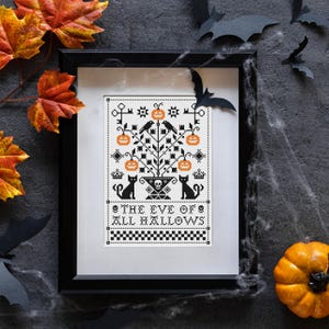 Könnte beinhalten: Ein gerahmtes Kreuzstichmuster mit einem schwarz-orangen Design eines Baumes mit Kürbissen, zwei schwarzen Katzen und einem Totenkopfmotiv. Der Text lautet THE EVE OF ALL HALLOWS, ergänzt durch eine karierte Bordüre am unteren Bildrand.