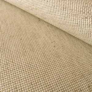 May include: A roll of light beige fabric featuring a distinct, coarse, and open-weave texture. The material displays a grid-like pattern created by thick, interlaced fibers, with one section folded over to reveal the consistent weave of the textile.