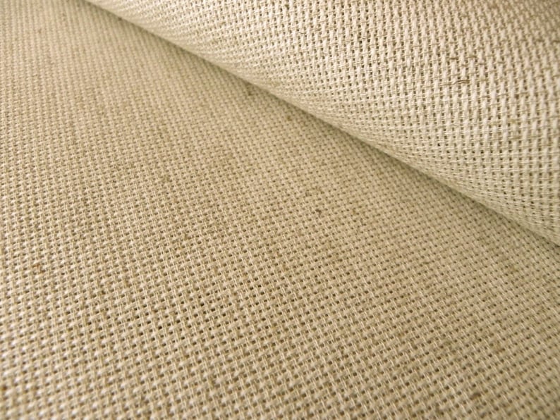 May include: A roll of light beige fabric featuring a distinct, coarse, and open-weave texture. The material displays a grid-like pattern created by thick, interlaced fibers, with one section folded over to reveal the consistent weave of the textile.