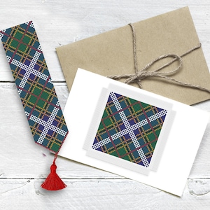 May include: A green, blue, white, and red plaid bookmark with a red tassel. The bookmark is on a white wooden surface next to a white card with a smaller version of the bookmark on it.