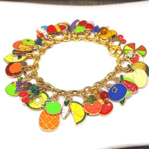 May include: A gold-toned charm bracelet featuring colorful enamel fruit charms. The charms include a pineapple, lemon, strawberry, and other fruits. The bracelet is a fun and vibrant accessory.