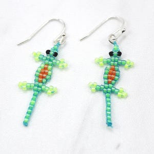 May include: A pair of silver dangle earrings featuring green, orange, and black beaded lizard charms.