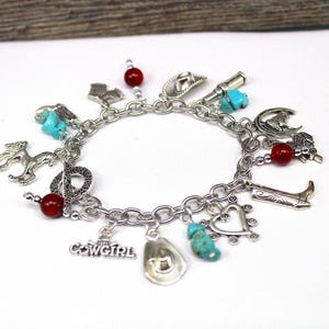 May include: Silver charm bracelet with cowboy-themed charms, including a cowboy hat, boot, horse, and the word "Cowgirl." Accented with turquoise and red beads. A western-themed accessory.