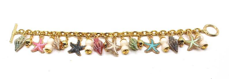 K&ouml;nnte beinhalten: Ein goldenes Kettenarmband mit mehreren Anh&auml;ngern, darunter Muscheln, Seesterne und Perlen. Die Anh&auml;nger sind in verschiedenen Farben, darunter rosa, blau, gr&uuml;n und wei&szlig;.