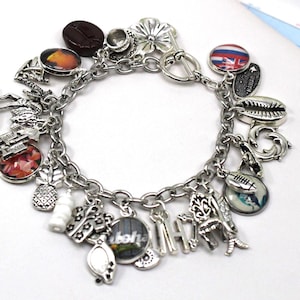 May include: Silver charm bracelet featuring various charms, including a coffee bean, flower, and a charm with the Hawaiian flag. Other charms include a pineapple, a shell, and the word "Aloha".