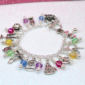 May include: A silver charm bracelet with a variety of charms, including a teacup, a rose, a clock, a bow, and a princess. The charms are attached to a silver chain with small silver beads.