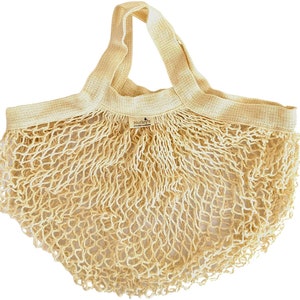 May include: A beige cotton mesh produce bag with a wide, flat handle. The bag has a small label that reads "Nutley's Kitchen Garden".