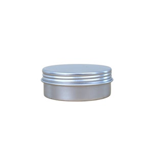 May include: A silver metal tin with a rounded lid. The lid has three ridges around the edge.