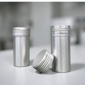 Könnte beinhalten: Drei Behälter aus gebürstetem Aluminium mit Schraubdeckeln. Zwei stehen aufrecht, und ein Deckel liegt zur Seite. Die Behälter sind zylindrisch mit einem geriffelten Design auf den Deckeln. Der Hintergrund ist unscharf.