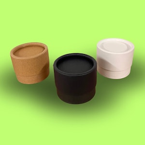Op de afbeelding: Drie kartonnen containers, een bruin, een zwart en een wit. De containers zijn cilindrisch en hebben een gladde, matte afwerking.