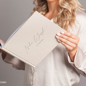 May include: A natural linen wedding guest book with the text "Nadia & Joseph 18th May 2024" in black calligraphy.