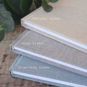 May include: Three linen-covered journals stacked on top of each other. The top journal is natural linen, the middle journal is grey linen, and the bottom journal is blue-grey linen.