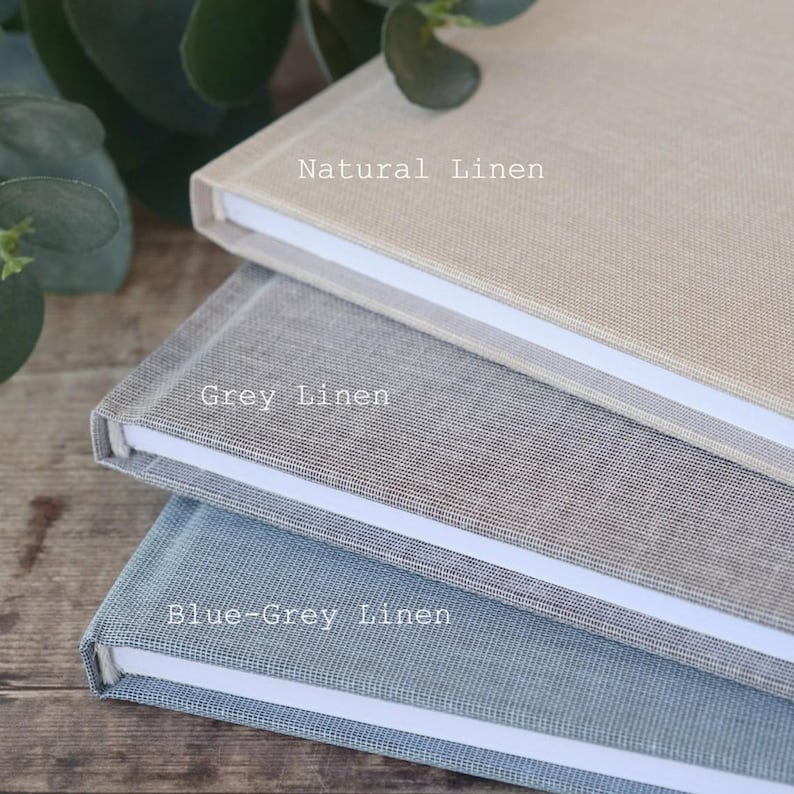 May include: Three linen-covered journals stacked on top of each other. The top journal is natural linen, the middle journal is grey linen, and the bottom journal is blue-grey linen.