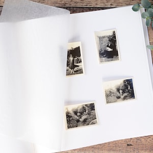 May include: A white photo album with four black and white photos inserted. The photos are of people and landscapes.