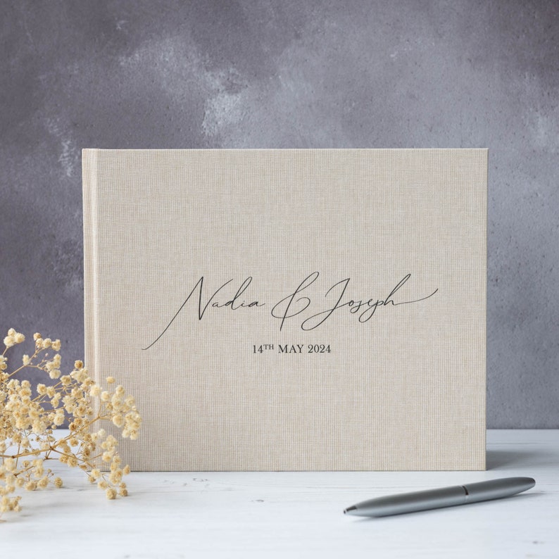 May include: A beige linen guest book with the text "Nadia & Joseph" in cursive script and the date "14th MAY 2024" printed below.