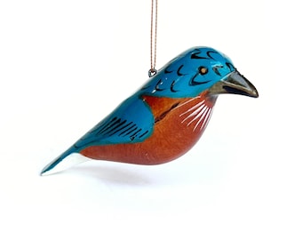 May include: A blue and brown wooden bird ornament with a white belly. The bird has a black eye and a black beak. The ornament is hanging from a brown string.